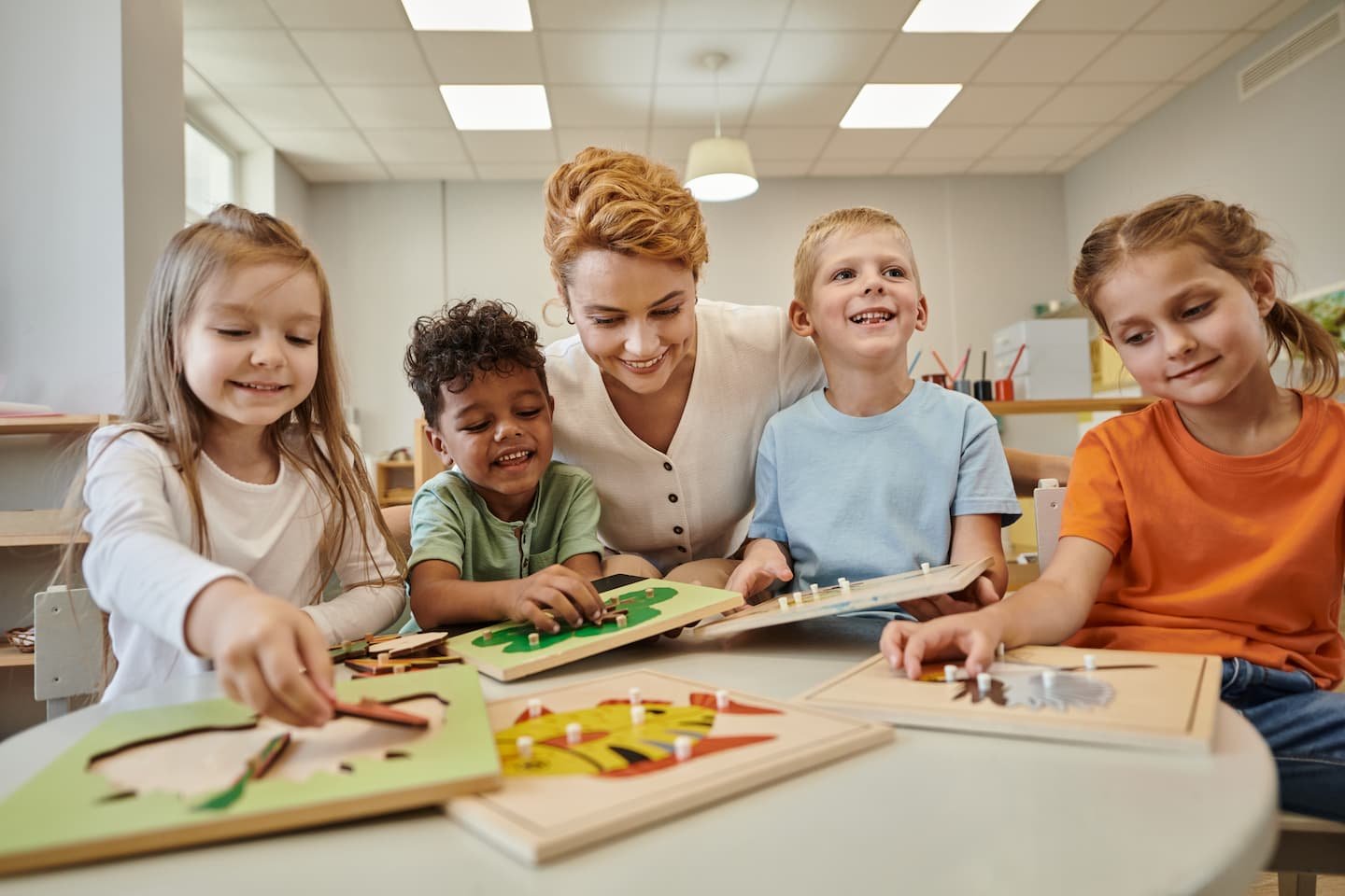 cheerful-teacher-sitting-near-multiethnic-kids-pla-QTNTDRN.jpg
